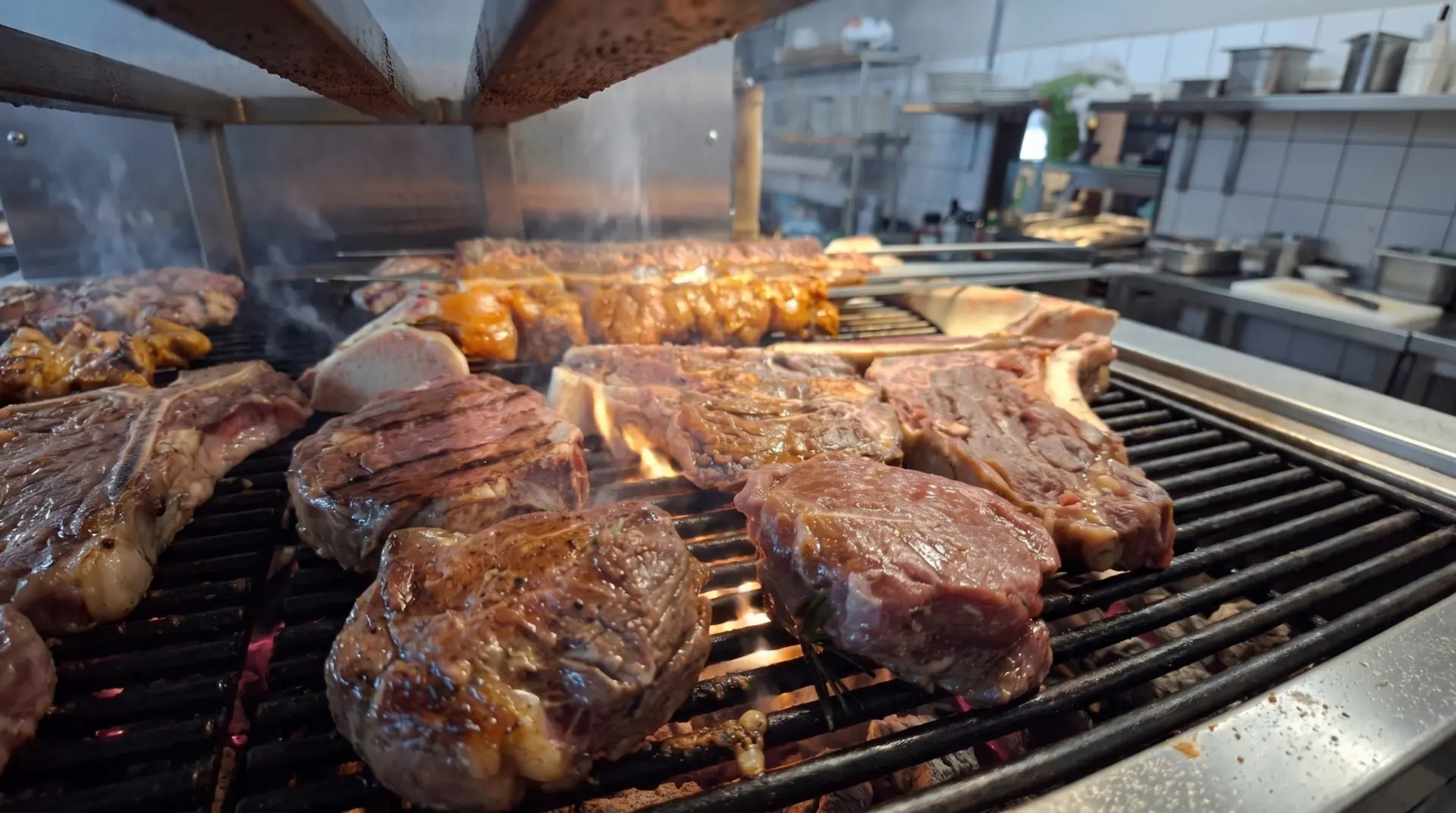 Kjøtt tett på flammene og røyken over grillristen, med kjøkkenet i bakgrunnen.